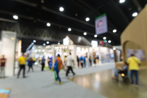 Vaste hall d'exposition avec visiteurs circulant entre stands commerciaux blancs